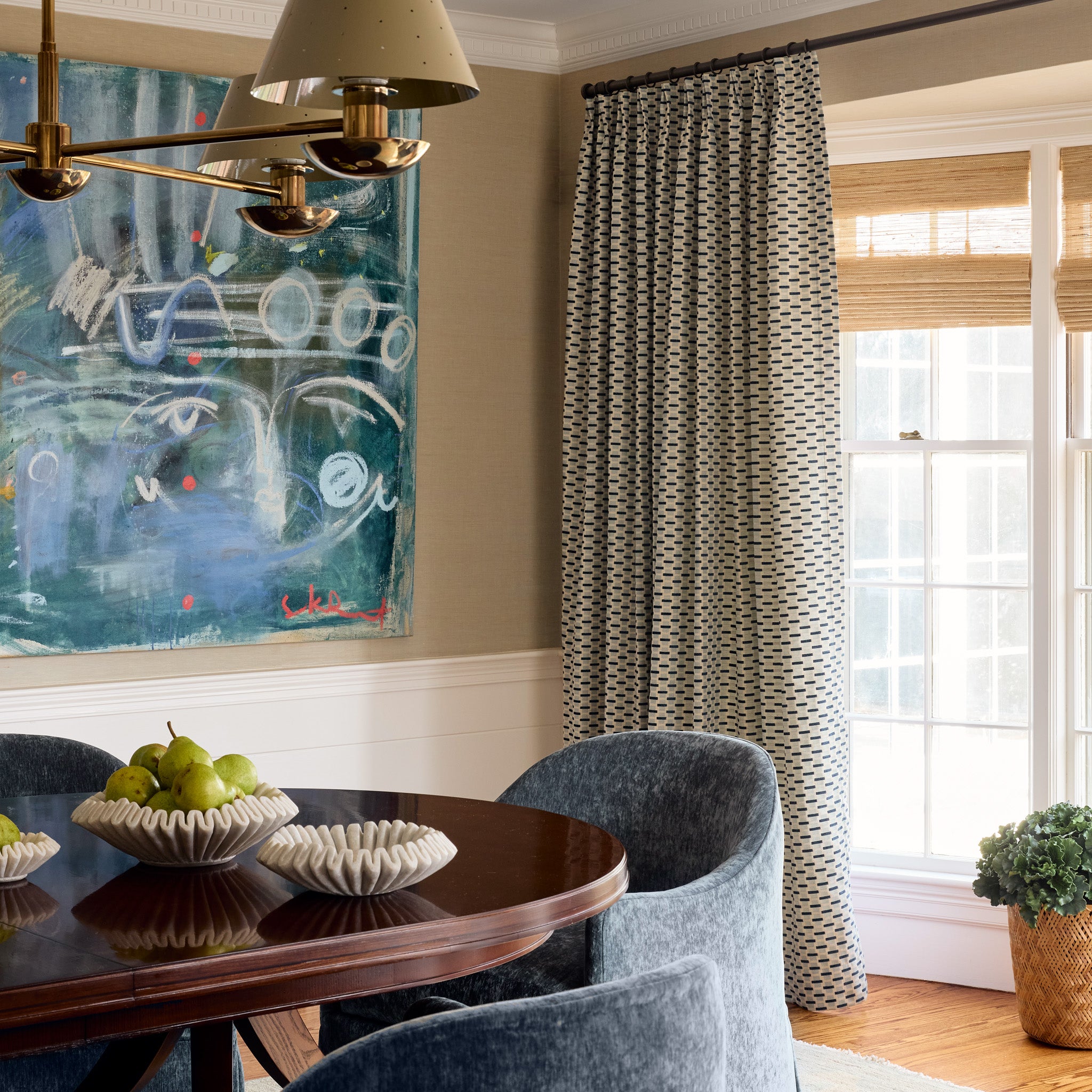 blue abstract geometric curtain on a metal rod in front of an illuminated window in a dining room with a dark wood table and blue chairs